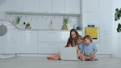 Moderne-Wohnung-Mutter-Und-Zwei-Söhne-Sitzen-Auf-Dem-Boden-Im-Wohnzimmer-Und-Schauen-Auf-Den-Laptop-Bildschirm